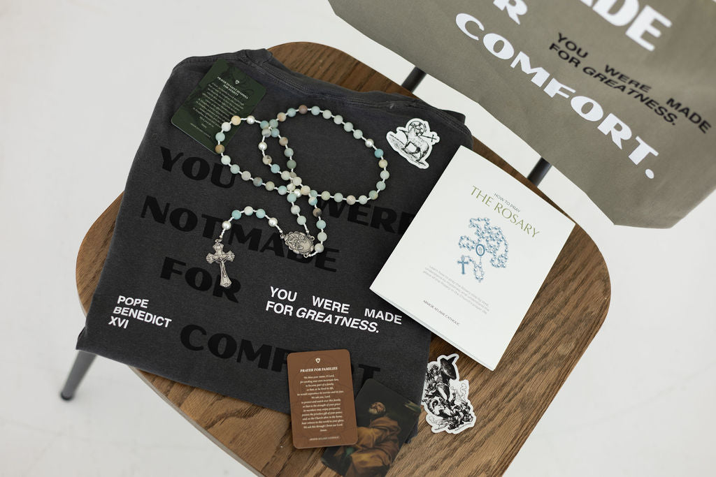 Black t-shirt with printed text, rosary, and cards on a wooden surface